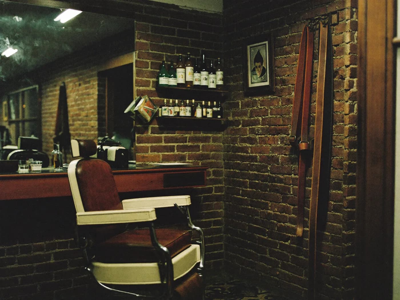 A characterful British barbershop interior: exposed brick, a worn leather chair and a shelf of bottles